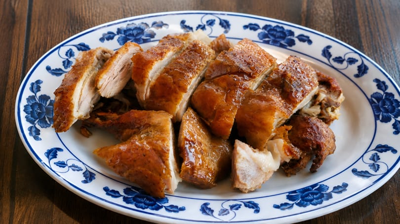 Sliced roasted chicken with crispy skin and glistening sauce on a white plate with blue floral patterns.